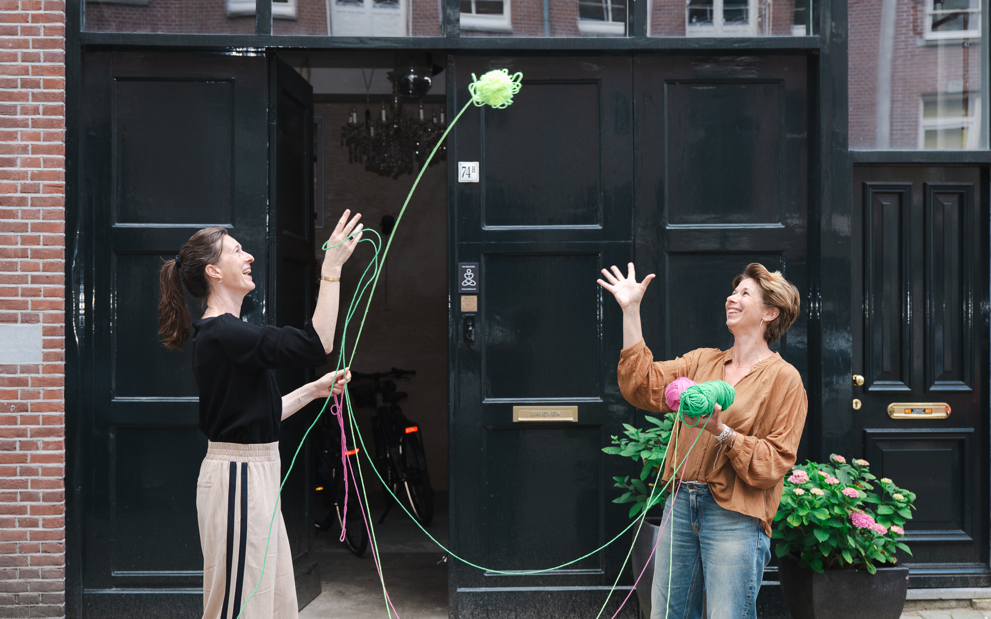 Katja en Ragini gooien samen een bol wol voor een deuropening